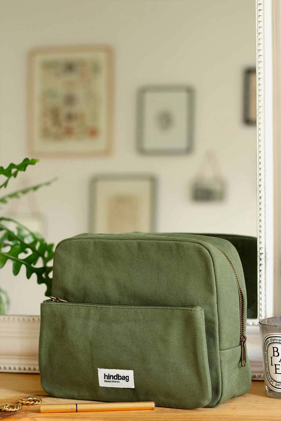 Trousse de toilette Hindbag Alix en coton bio vert olive avec poche zippée, posée sur une coiffeuse en bois devant un miroir. Accessoire éthique, pratique et durable pour le quotidien.