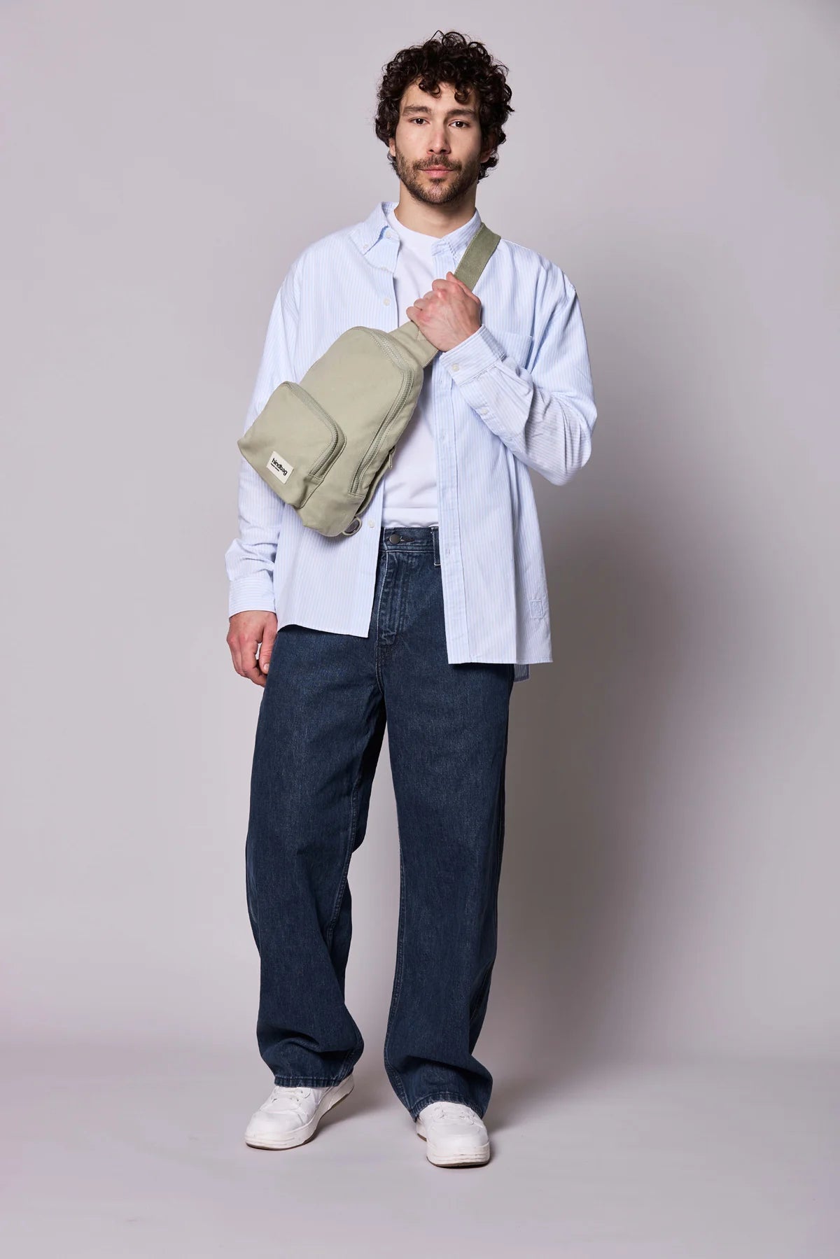 Hindbag Sling Bag Felix coloris Argile porté en bandoulière par un homme, sac compact unisexe au style urbain et pratique