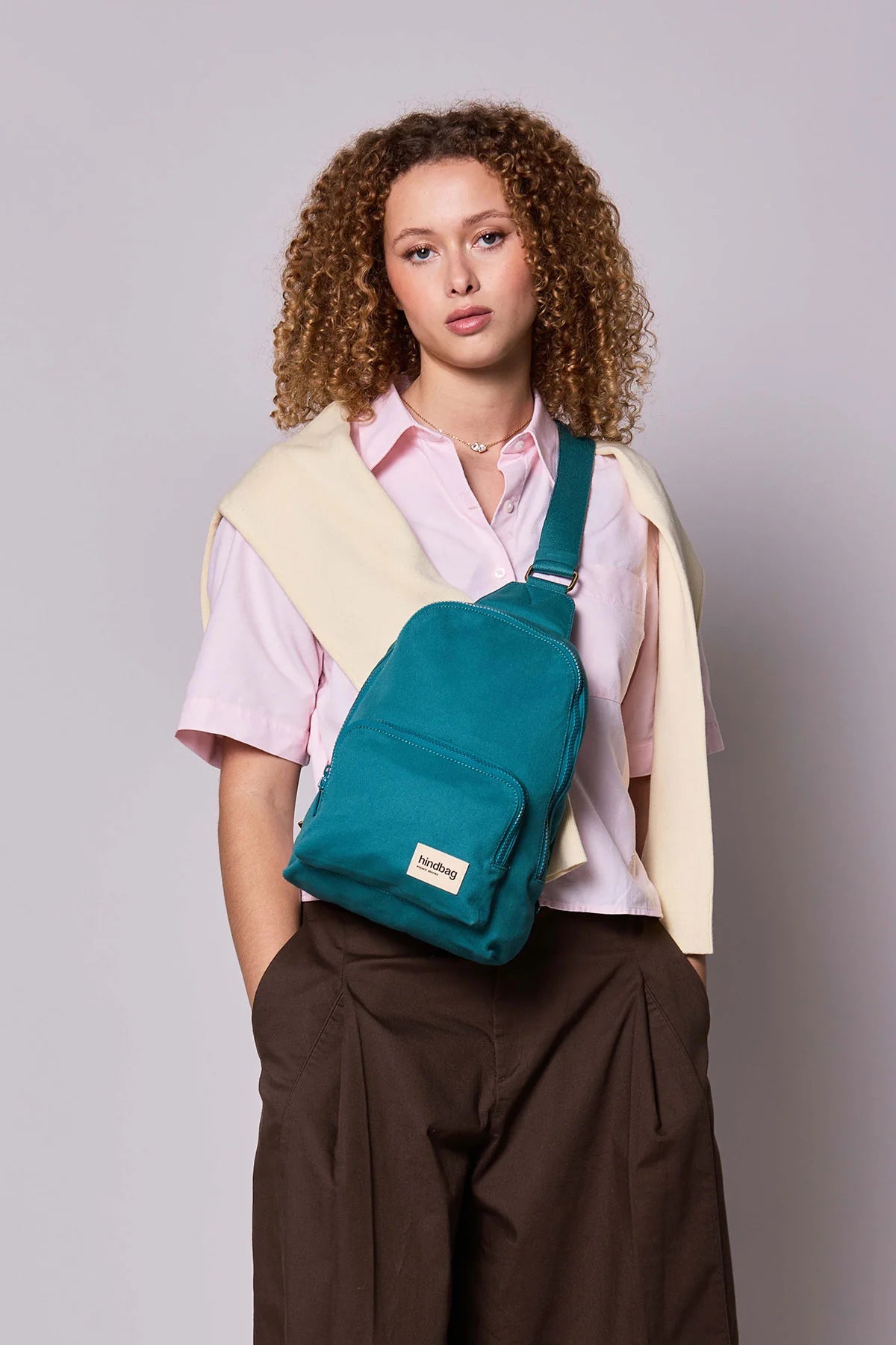 Hindbag Sling Bag Felix coloris Bleu Paon porté en bandoulière par une femme, sac compact unisexe au style urbain et pratique