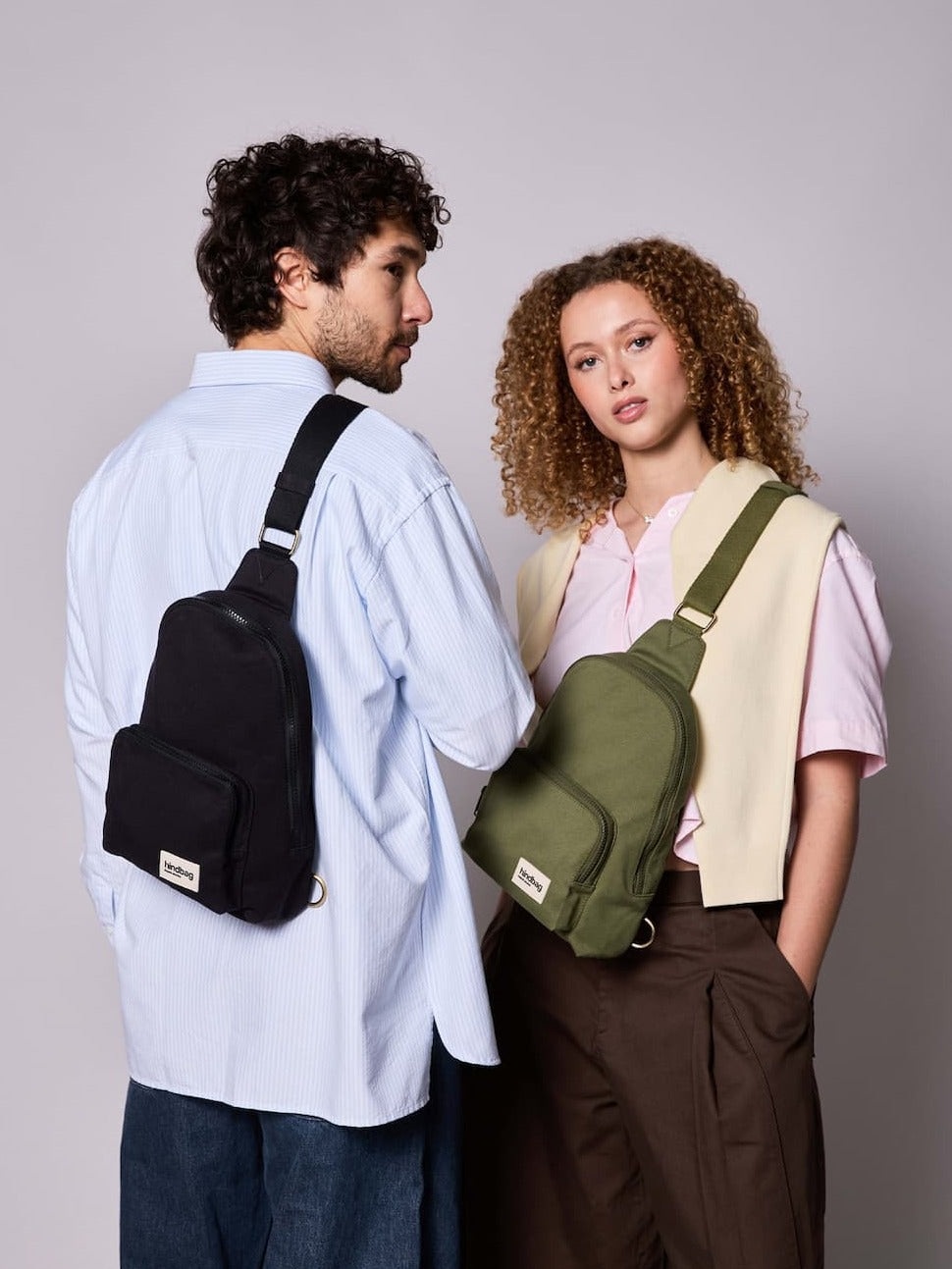 Hindbag Sling Bag Felix porté en bandoulière par un homme et une femme, sac compact unisexe au style urbain et pratique