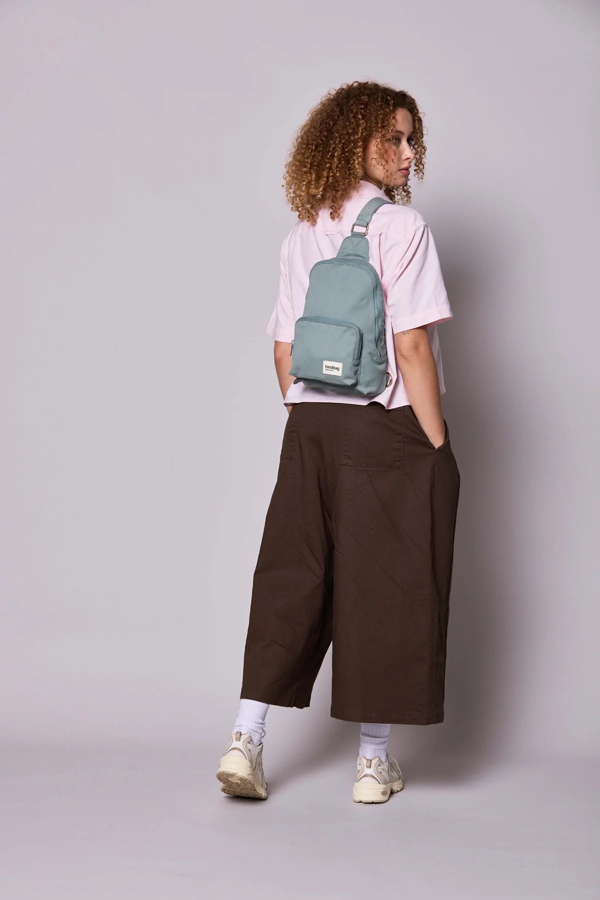 Hindbag Sling Bag Felix coloris Sauge porté dans le dos par une femme, sac compact unisexe au style moderne et pratique