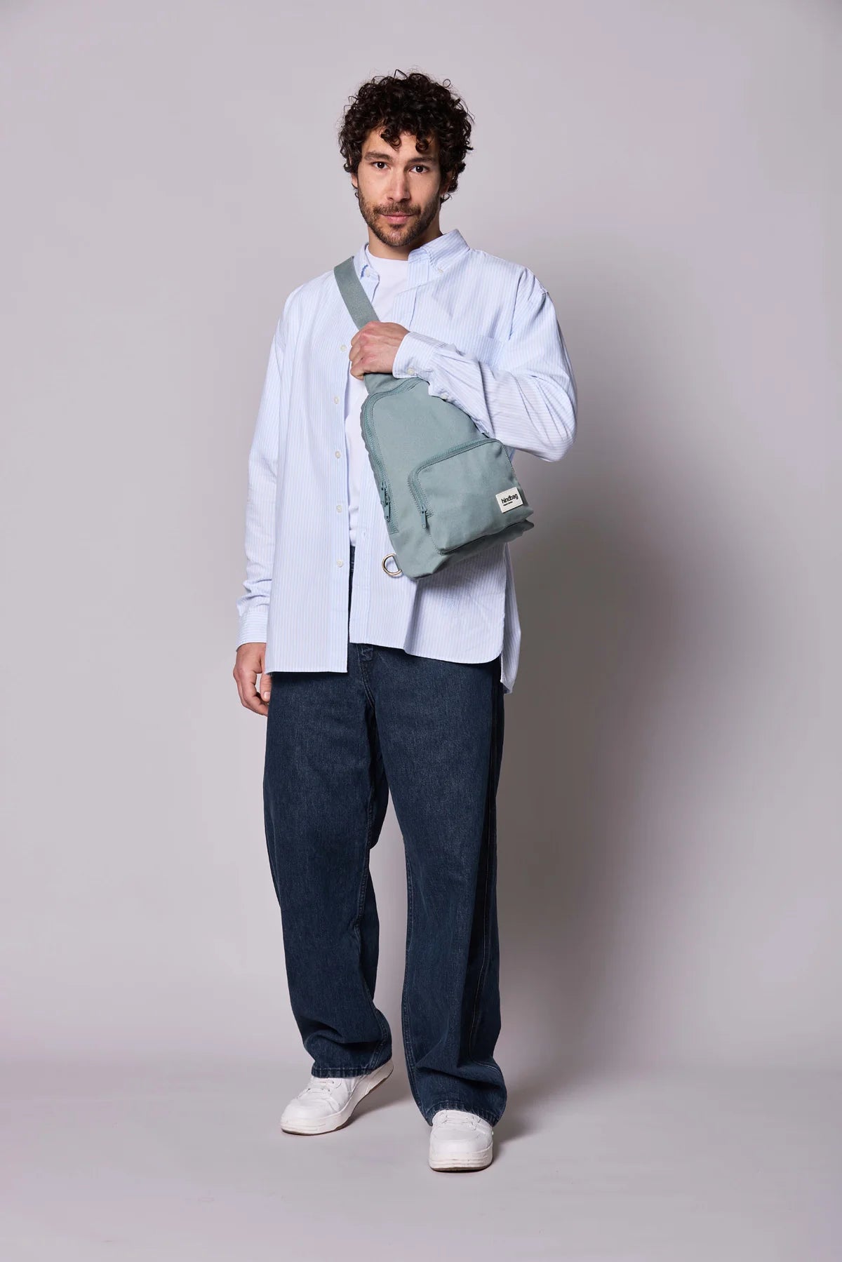 Hindbag Sling Bag Felix coloris Sauge porté en bandoulière par un homme, sac compact et ergonomique pour les déplacements du quotidien