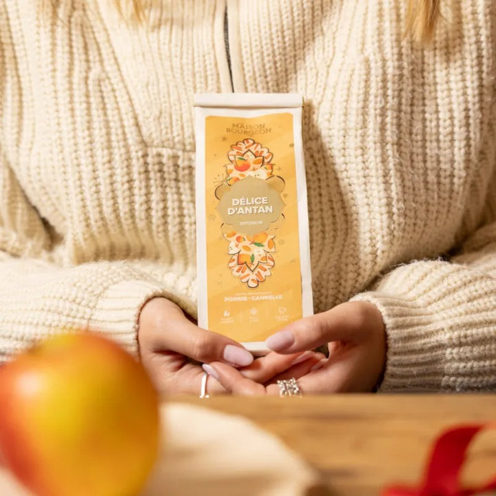 Infusion Délice d’Antan Maison Bourgeon tenue dans les mains, ambiance cocooning avec pull chaud