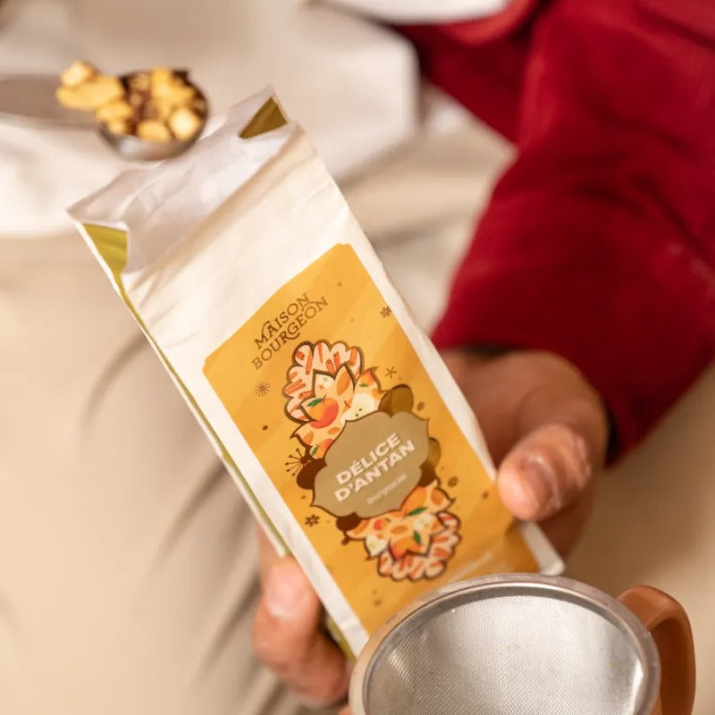 Sachet d’infusion Délice d’Antan Maison Bourgeon tenu à la main avec cuillère et filtre à thé