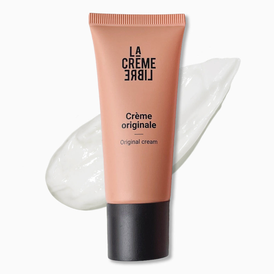 Crème Originale La Crème Libre en tube rose poudré, posée sur fond blanc avec texture visible appliquée en arrière-plan. Crème visage nourrissante à la texture onctueuse, idéale pour peau sèche.
