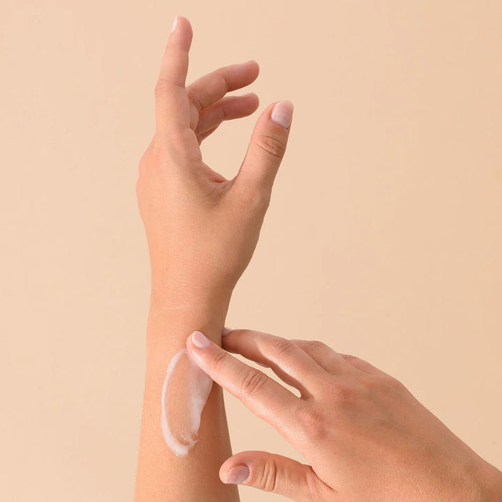 Application du Baume Magique Les Petits Prödiges sur l'avant-bras. Une main applique une noisette de baume sur la peau nue, montrant la texture du produit.
