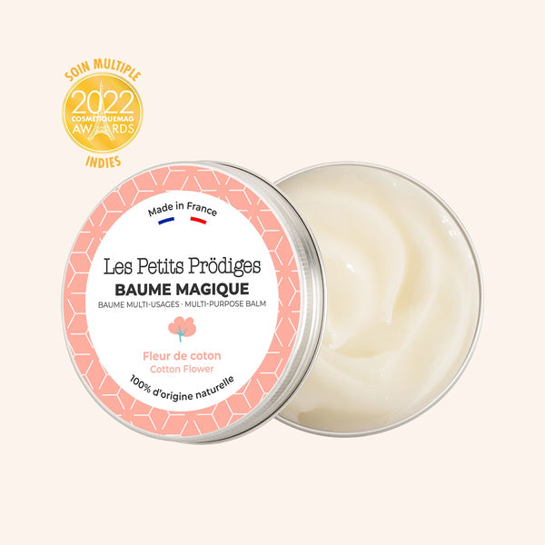Pot ouvert de Baume Magique Les Petits Prödiges avec étiquette rose et blanche, montrant une texture crémeuse à l'intérieur. Le produit est étiqueté "Made in France" avec un drapeau français, mentionnant "Fleur de coton" et "100% d'origine naturelle". Récompensé par les CosmetiqueMag Awards 2022.
