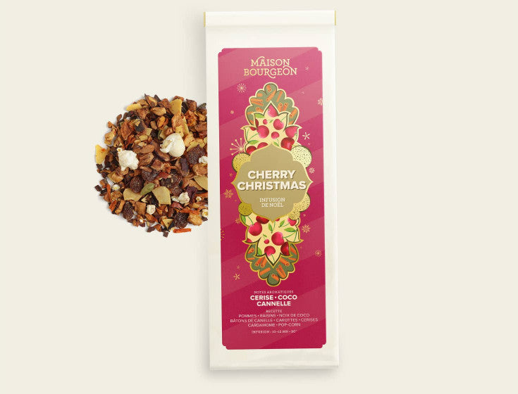 Image du produit Cherry Christmas de la marque Maison Bourgeon. L'emballage est rouge avec des motifs floraux, et le contenu de l'infusion, composé de pommes, raisins, noix de coco, bâtons de cannelle, carottes, cerises, cardamome et pop-corn, est visible à côté.