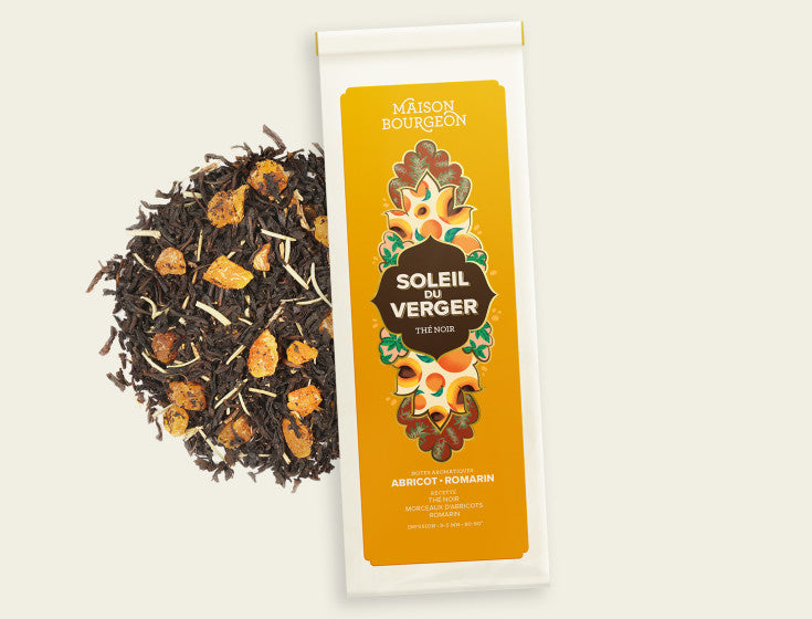 Paquet de thé noir Maison Bourgeon Soleil du Verger avec des morceaux de thé, d'abricots et de romarin disposés à côté du paquet.
