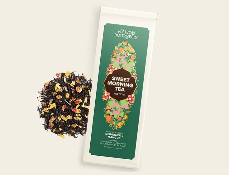 Image présentant le thé noir "Sweet Morning Tea" de la Maison Bourgeon. Le packaging élégant de couleur verte et décoré de motifs floraux met en avant les arômes de bergamote et de mangue. À côté du paquet, un mélange vibrant de feuilles de thé noir est agrémenté de pétales de rose, de tournesol et de bleuet, soulignant les ingrédients naturels et les notes aromatiques de cette infusion revigorante.