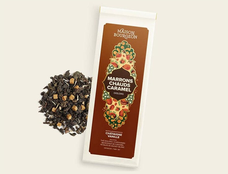 Image du produit "MARRONS CHAUDS CARAMEL" de la marque Maison Bourgeon, montrant un paquet de thé Oolong aromatisé avec des saveurs de châtaigne et de vanille. Le paquet est à côté d'un mélange de thé en vrac, mettant en valeur les morceaux de caramel et de châtaigne naturels visibles dans le thé.