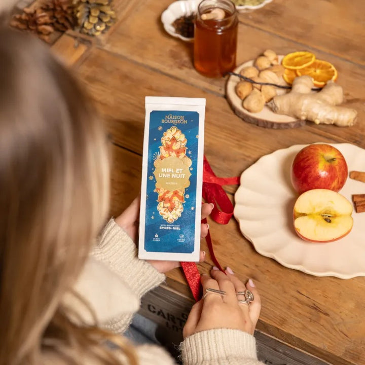 Sachet de rooibos Miel et une Nuit Maison Bourgeon tenu à la main sur une table avec pommes, miel et épices